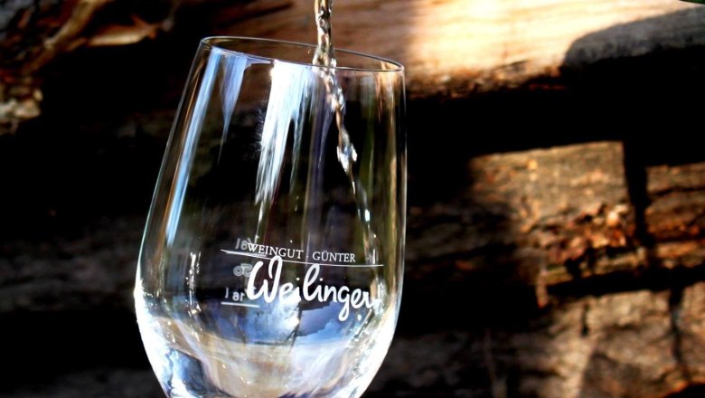 A glass of wine is poured from a bottle with an orange cap. Logs can be seen in the background.