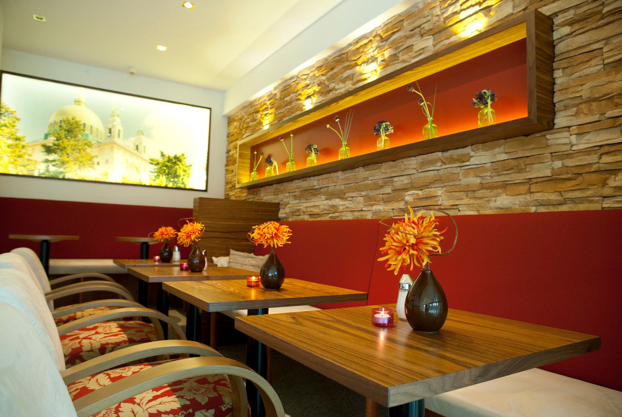 Interior view of a stylish day bar with wooden tables, red benches and decorative flower vases.