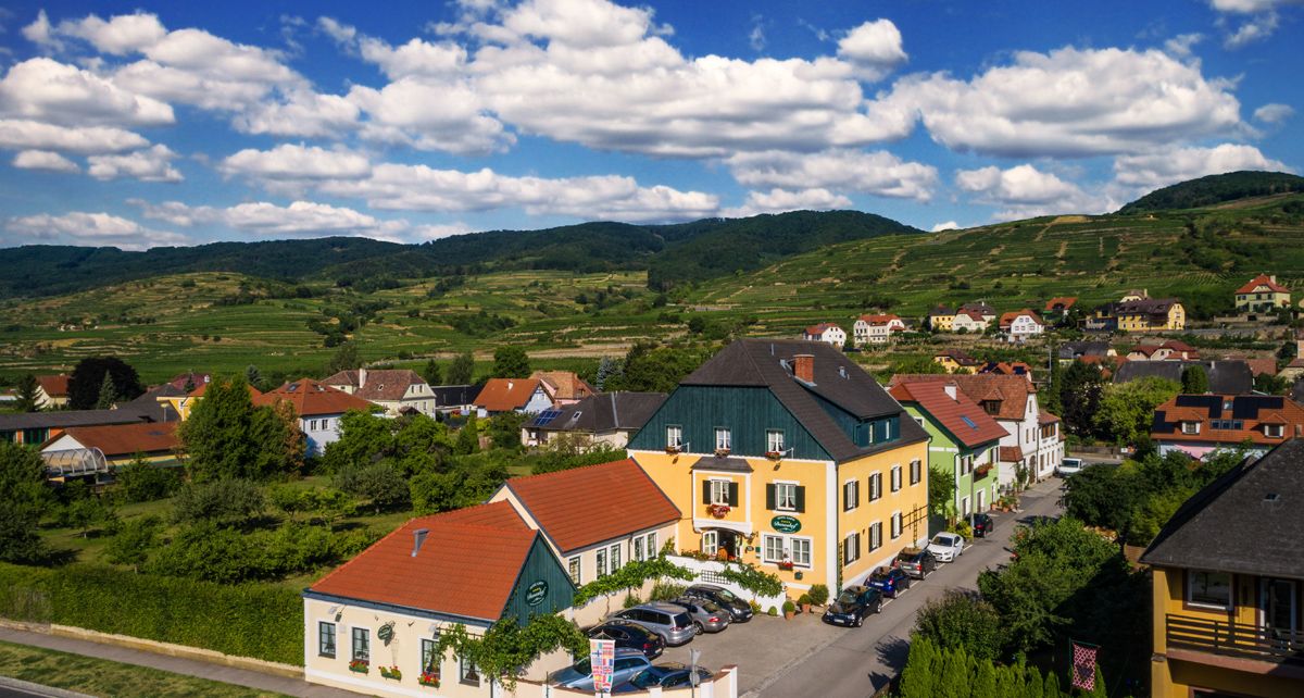 Rural houses in a green hilly landscape under a blue sky with clouds.