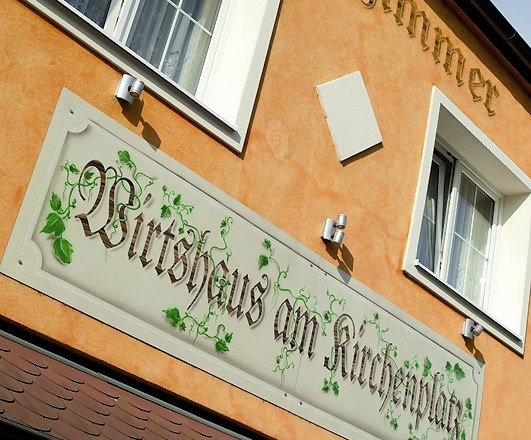 House, © Wirtshaus am Kirchenplatz Facade of a building with the sign 'Wirtshaus am Kirchenplatz'.