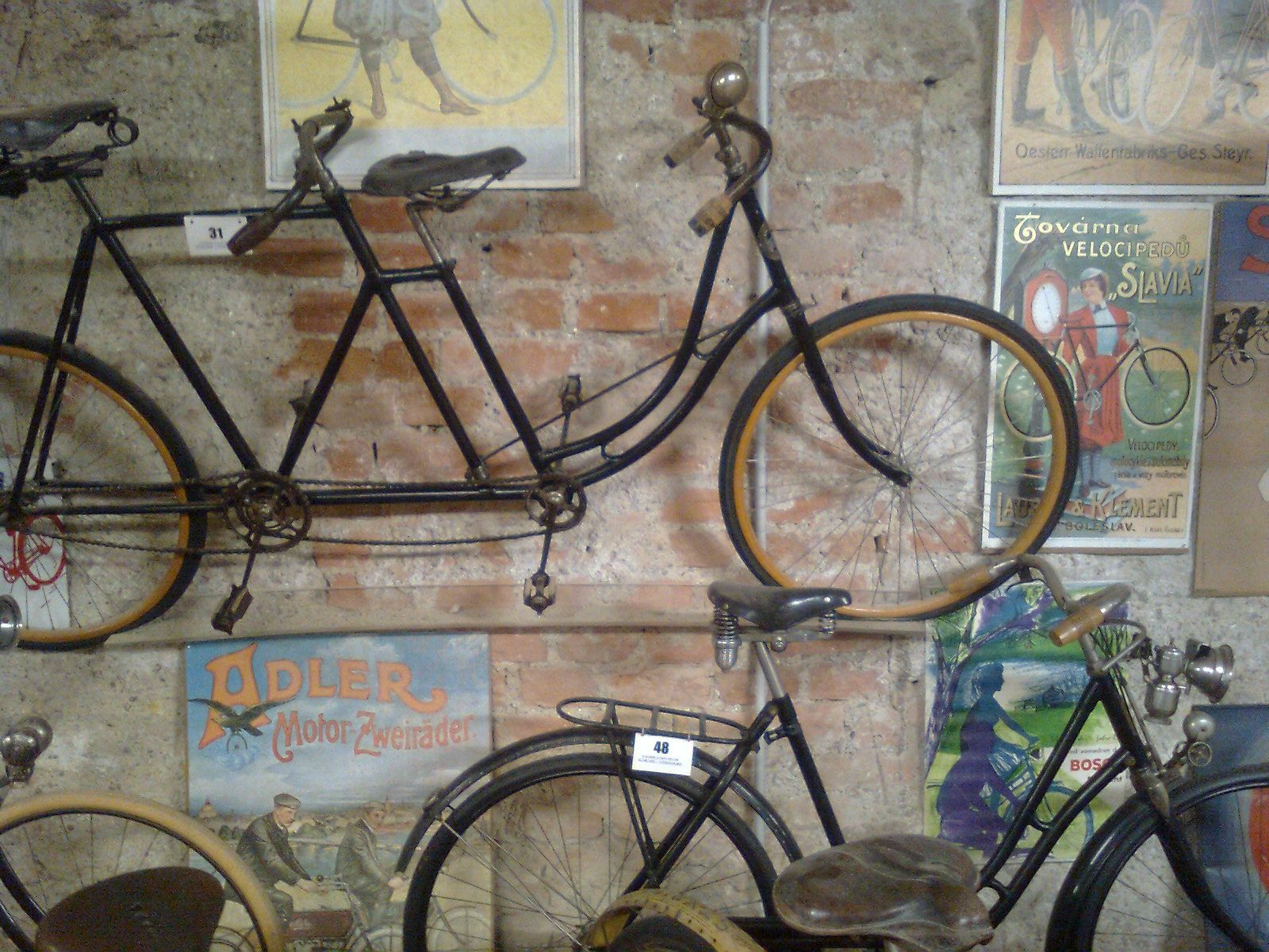 Old bicycles and vintage posters on a brick wall in the Vösendorf Castle Bicycle Museum.