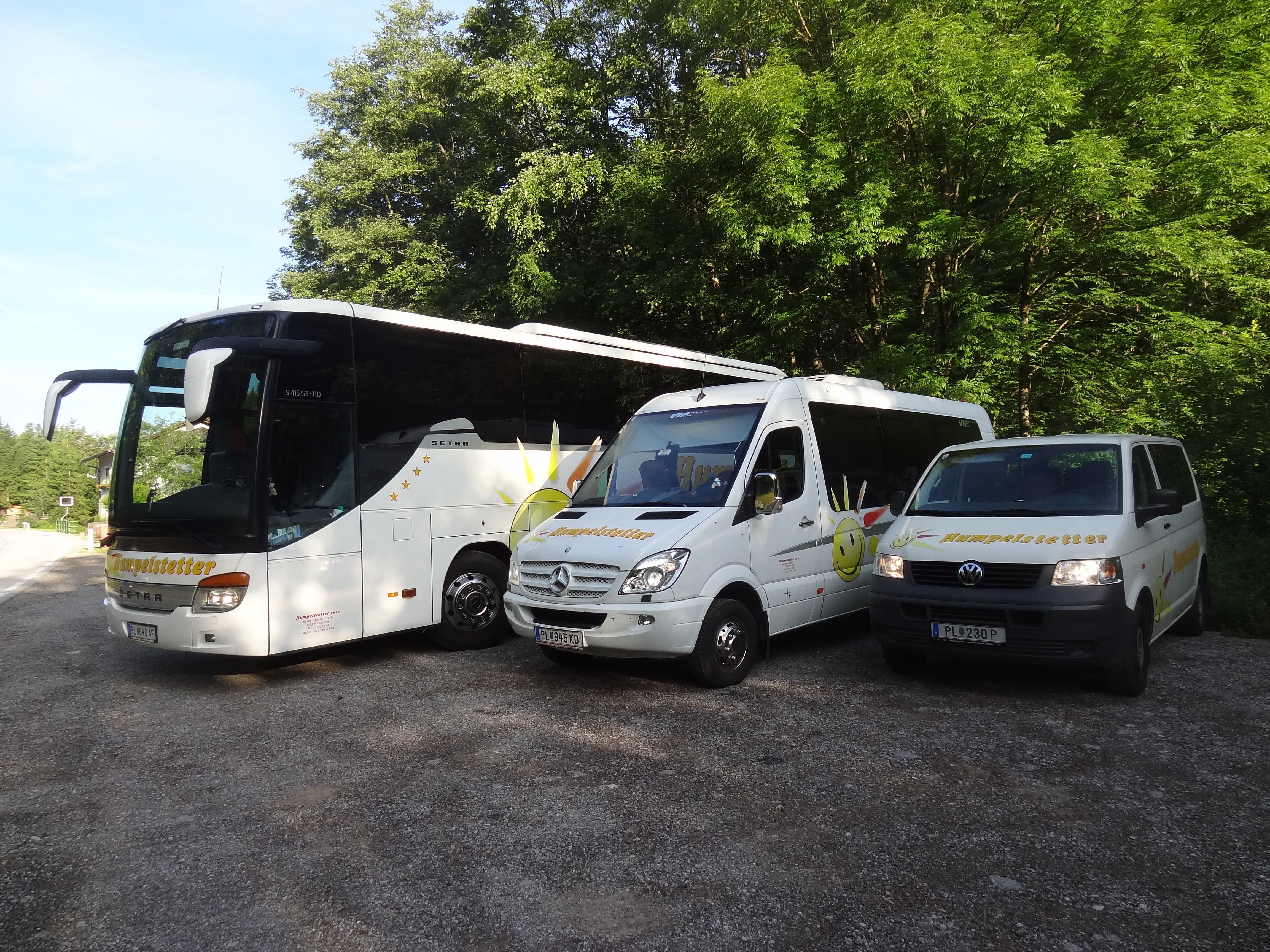 Three white vehicles with the Humpelstetter logo, parked on a gravel lot in front of trees.