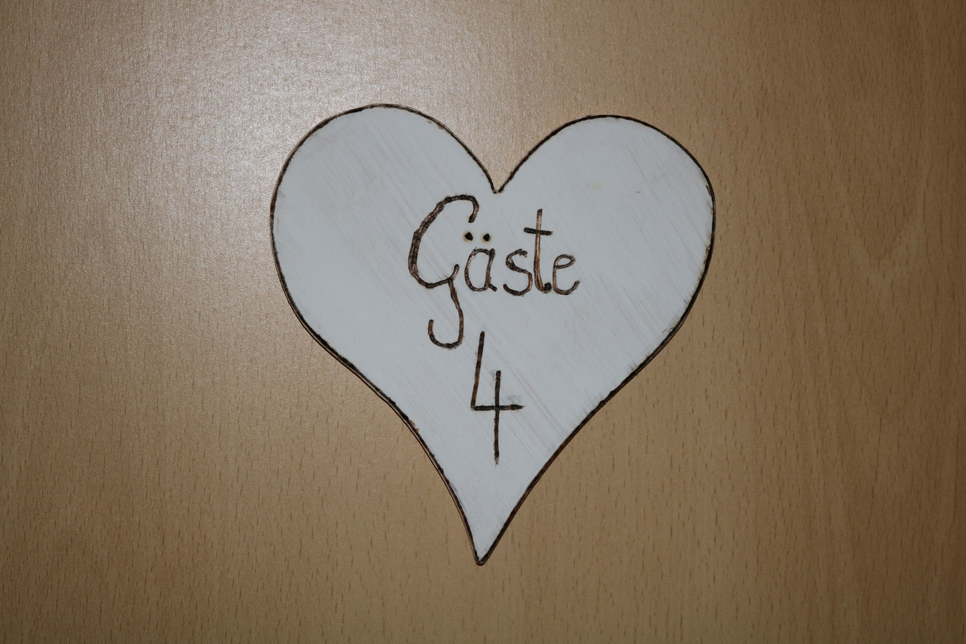 Wooden sign in the shape of a heart with the inscription 'Gäste 4'.
