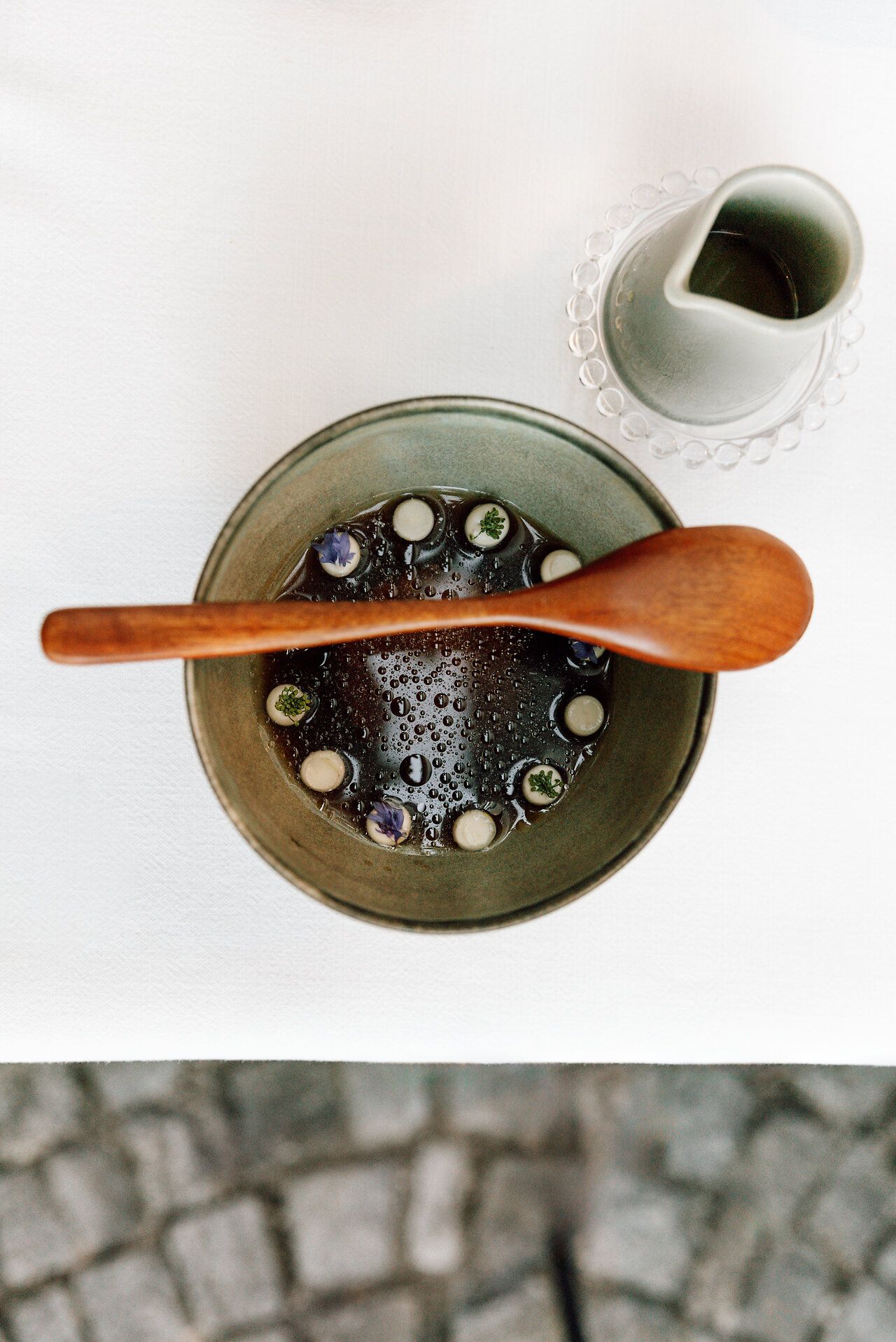 A person sits on a stool in a plain interior and looks into the camera