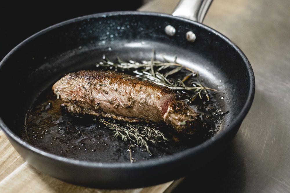 Roasted piece of meat with herbs in a pan.