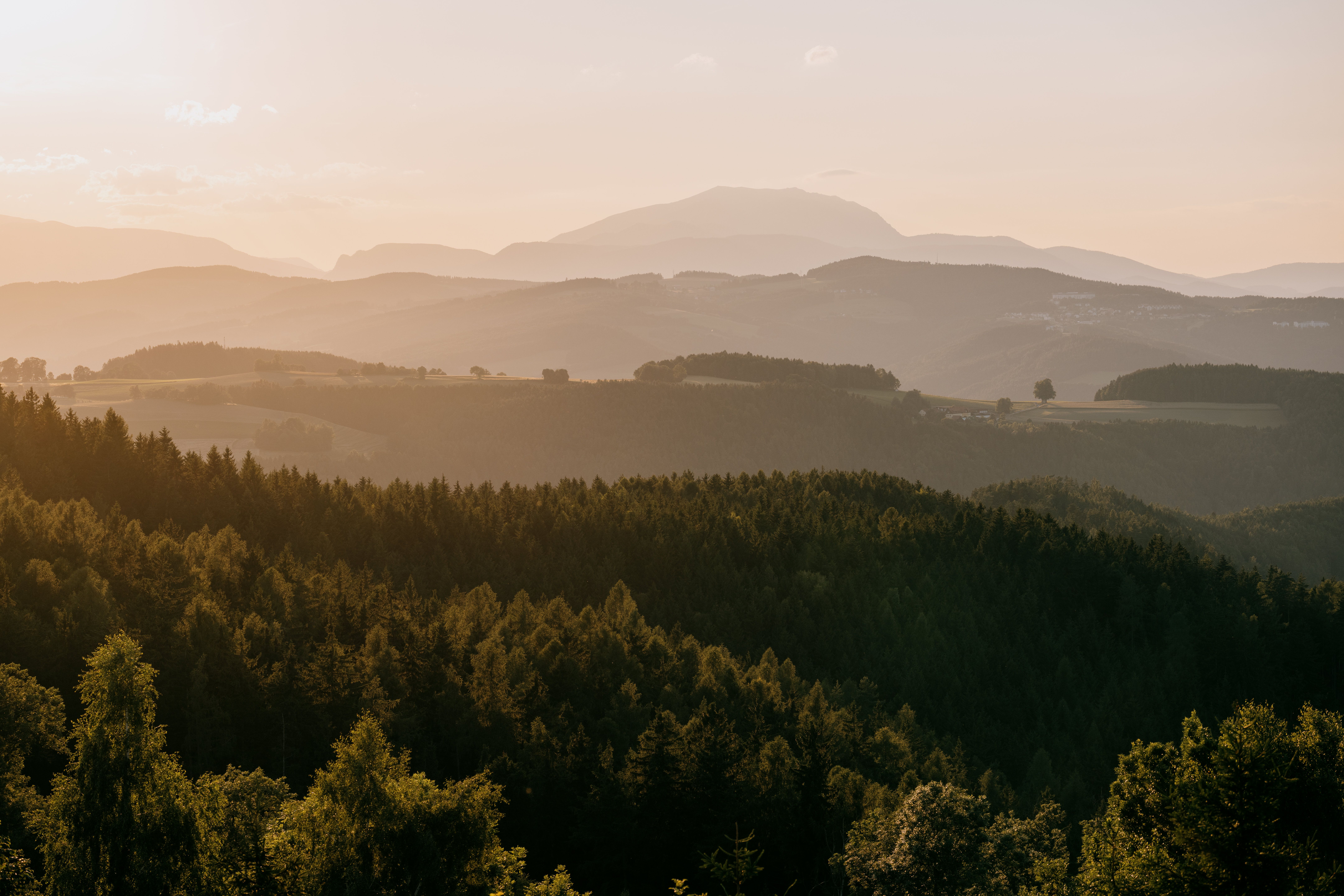 Sunset over a wooded hilly landscape with a snowy mountain in the background.