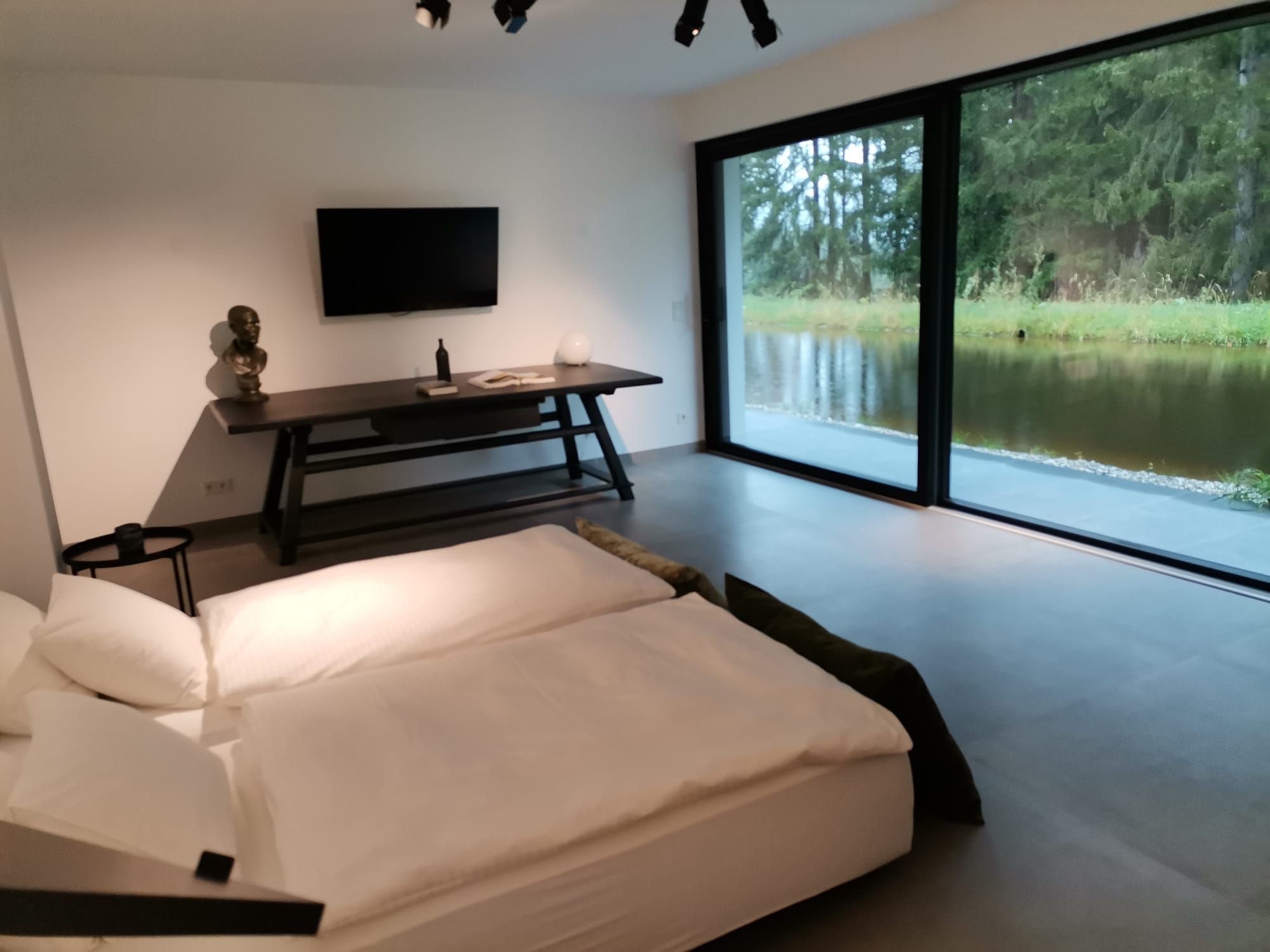Modern bedroom with large window and view of a pond.