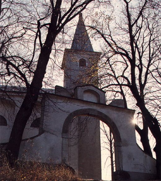 Church with tower and arch, surrounded by bare trees against the light.