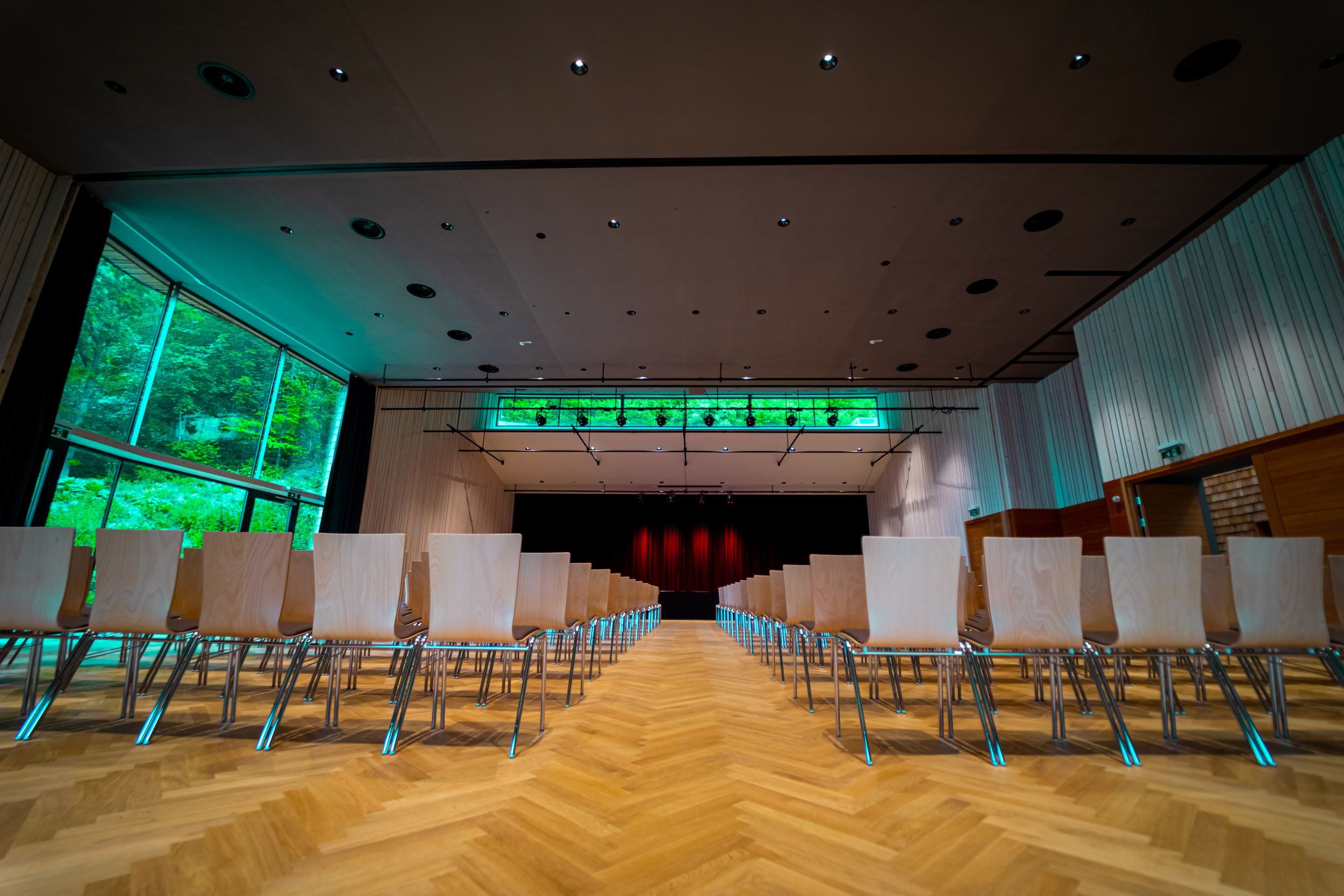 Interior view of a modern event room with empty rows of chairs and a stage in the background.