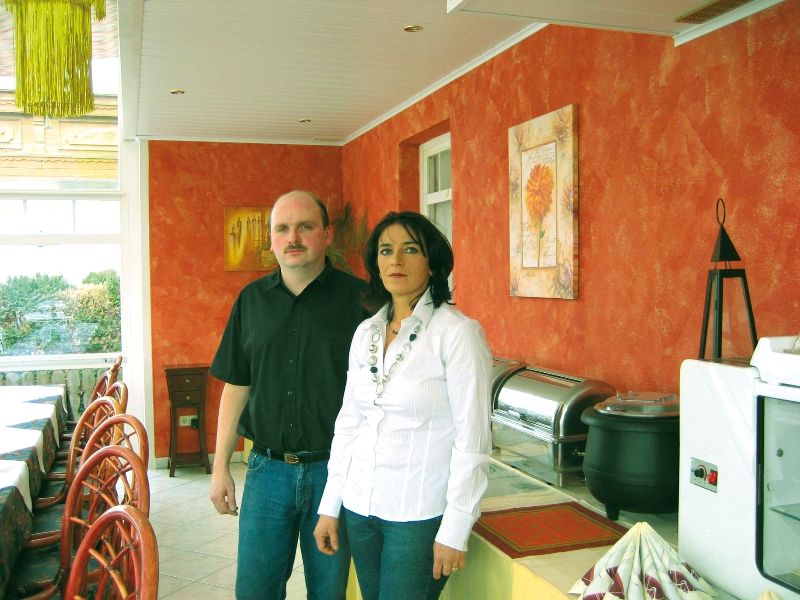 Two people are standing in a restaurant with orange-painted walls.