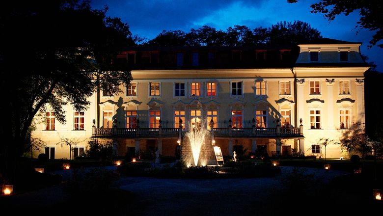 Illuminated Stuppach Castle at night with a fountain in the foreground.
