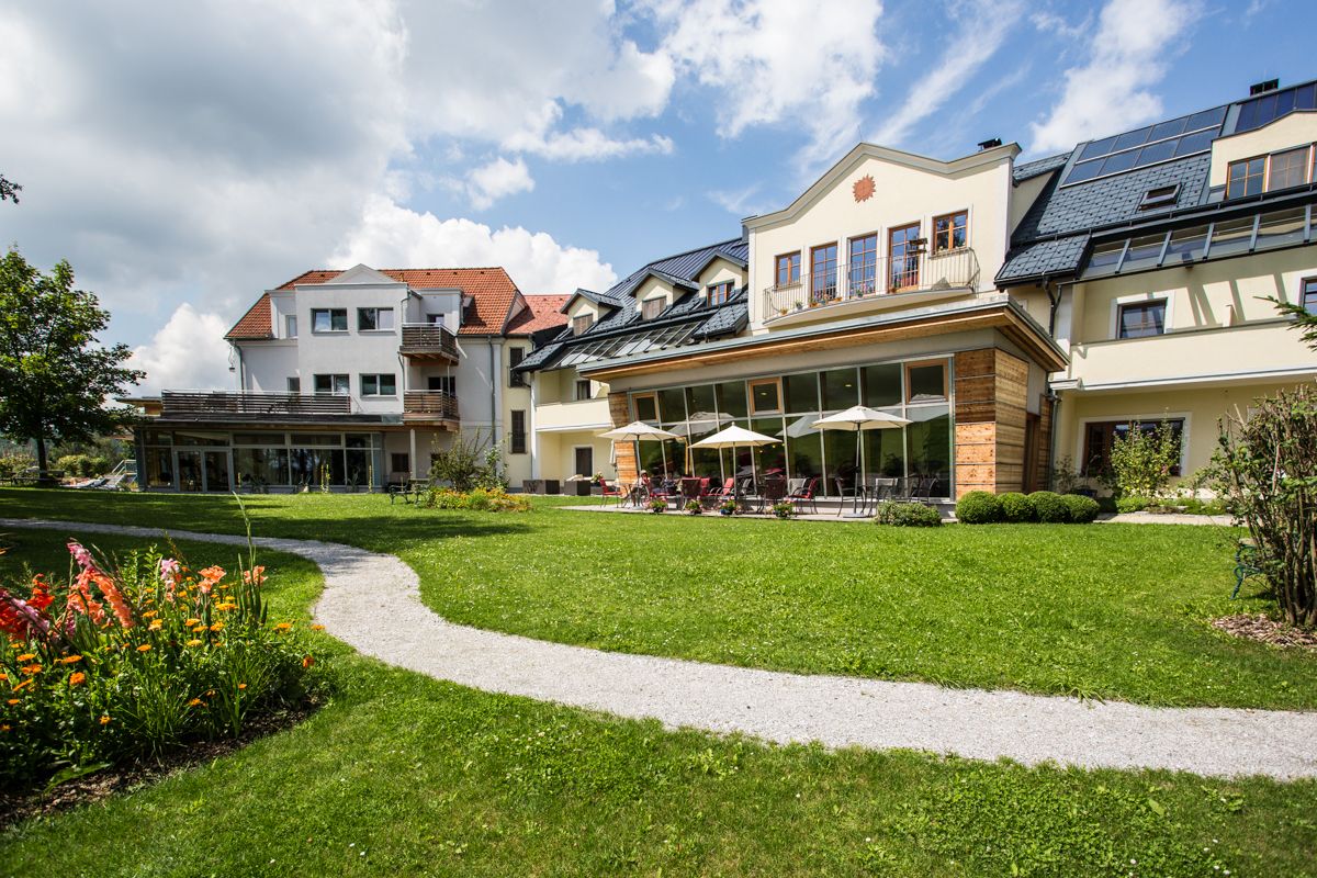 Large house with garden and terrace, surrounded by green meadows and flowers.