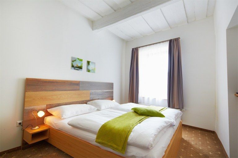 Bright bedroom with double bed, green bedspread and two small pictures on the wall.