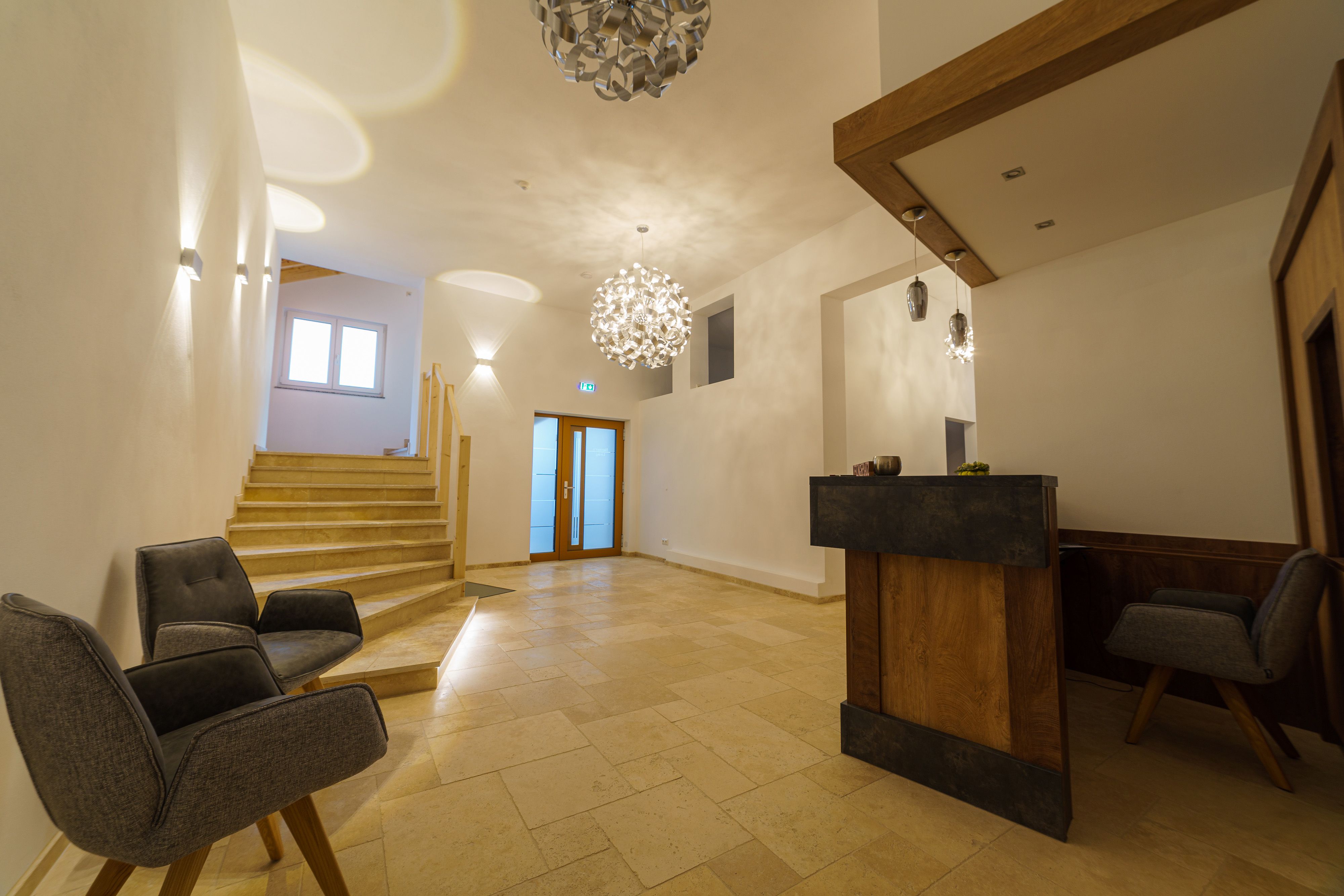 Modern reception with wooden counter, two gray armchairs and stairs.