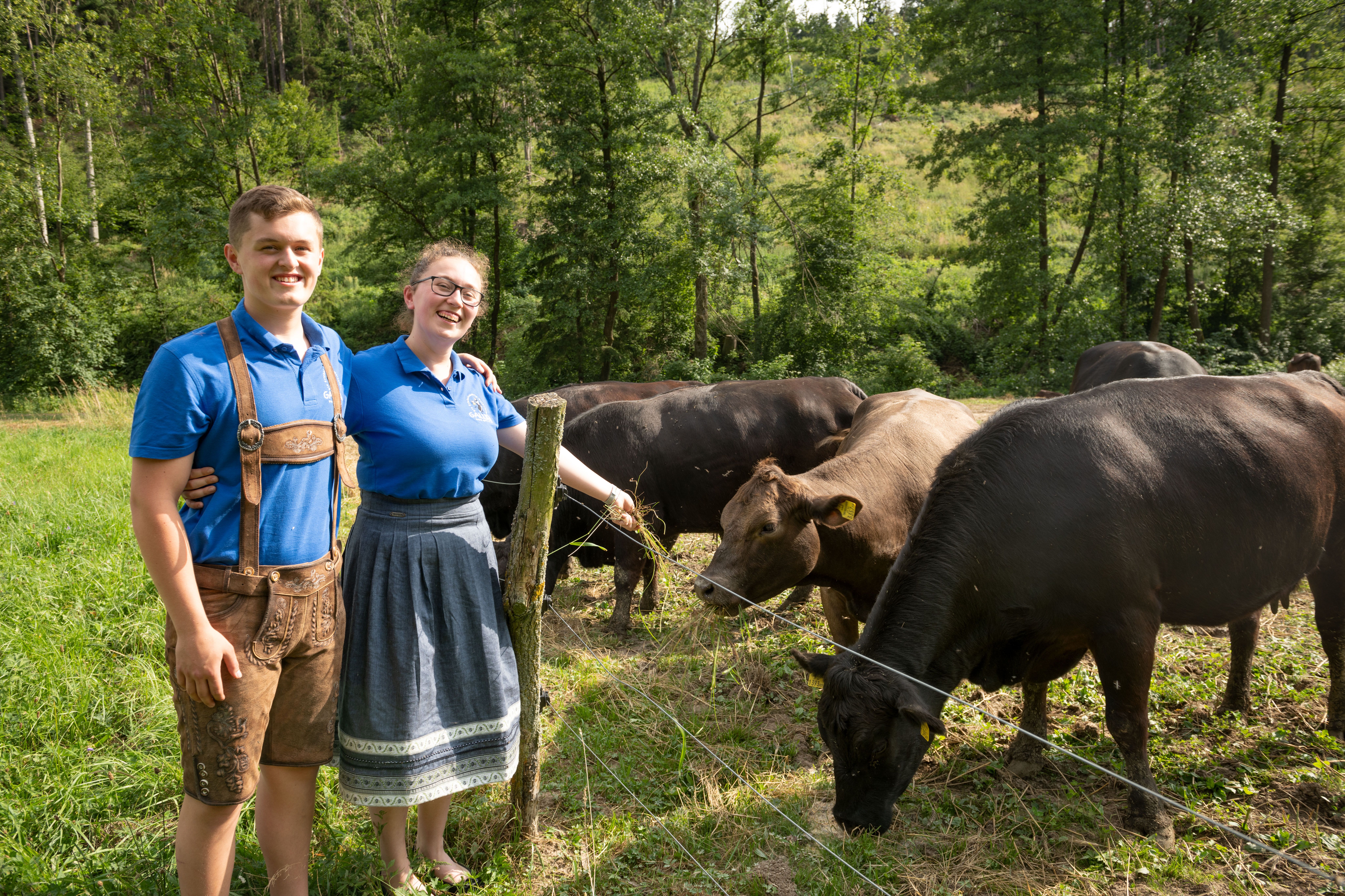 Two people in traditional clothing are standing next to a pasture with cows.