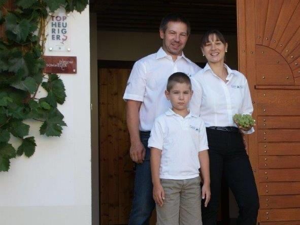 A family is standing in front of a building with a wooden door, the woman is holding grapes.