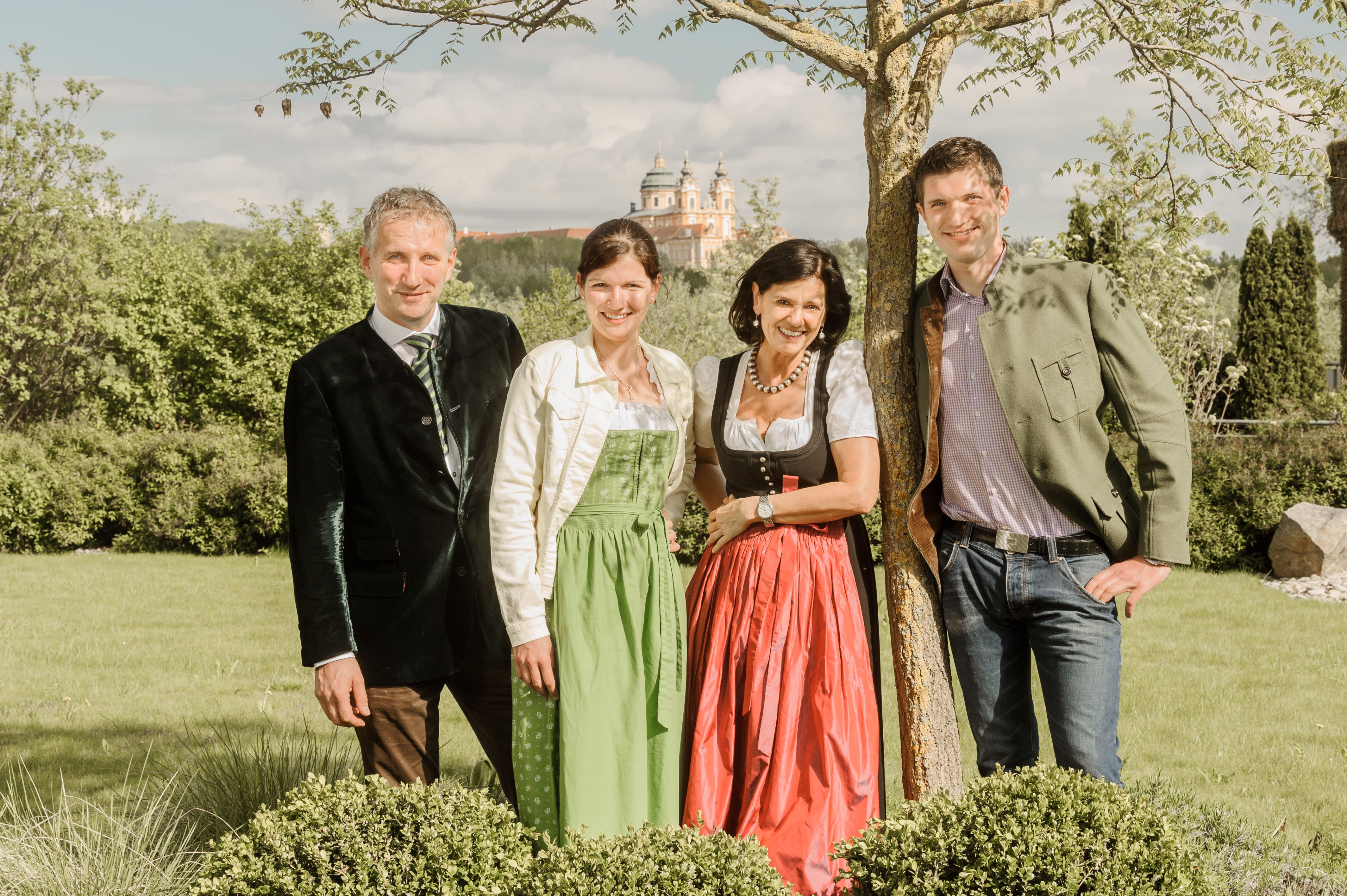 The Pichler family in traditional dress stand outside in front of a tree, with Sift Melk in the background