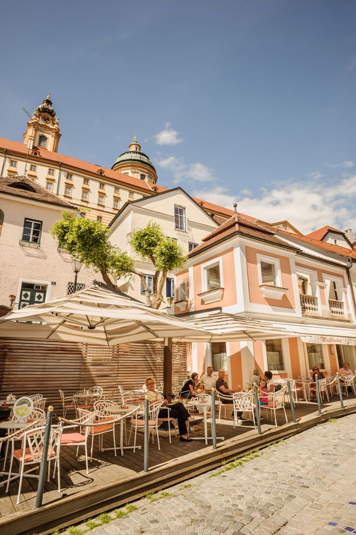 Outdoor area of a café with parasols and guests, in the background a historic building with a dome.