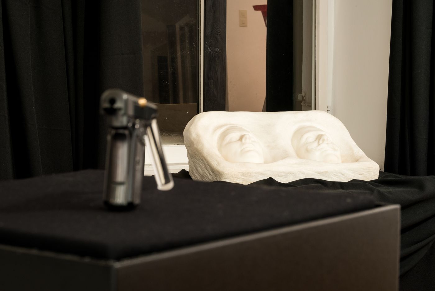 Sculpture with two faces and blurred object in the foreground.