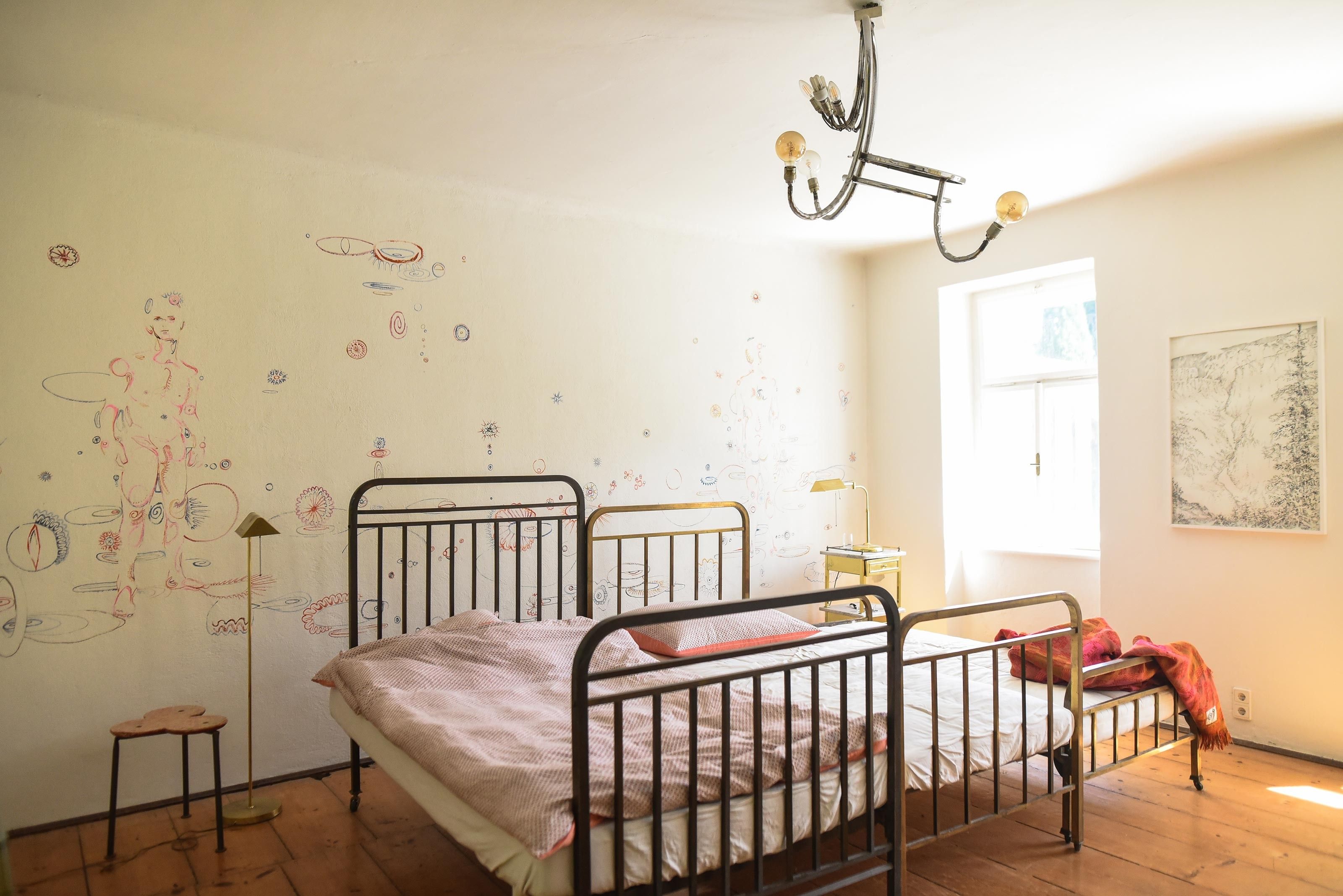 A bright bedroom with a metal bed, wall art, and a window that lets in natural light.