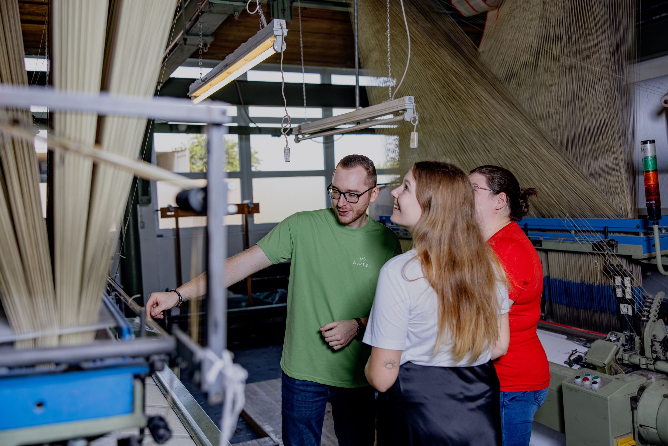 Three people in a textile factory look at a machine.