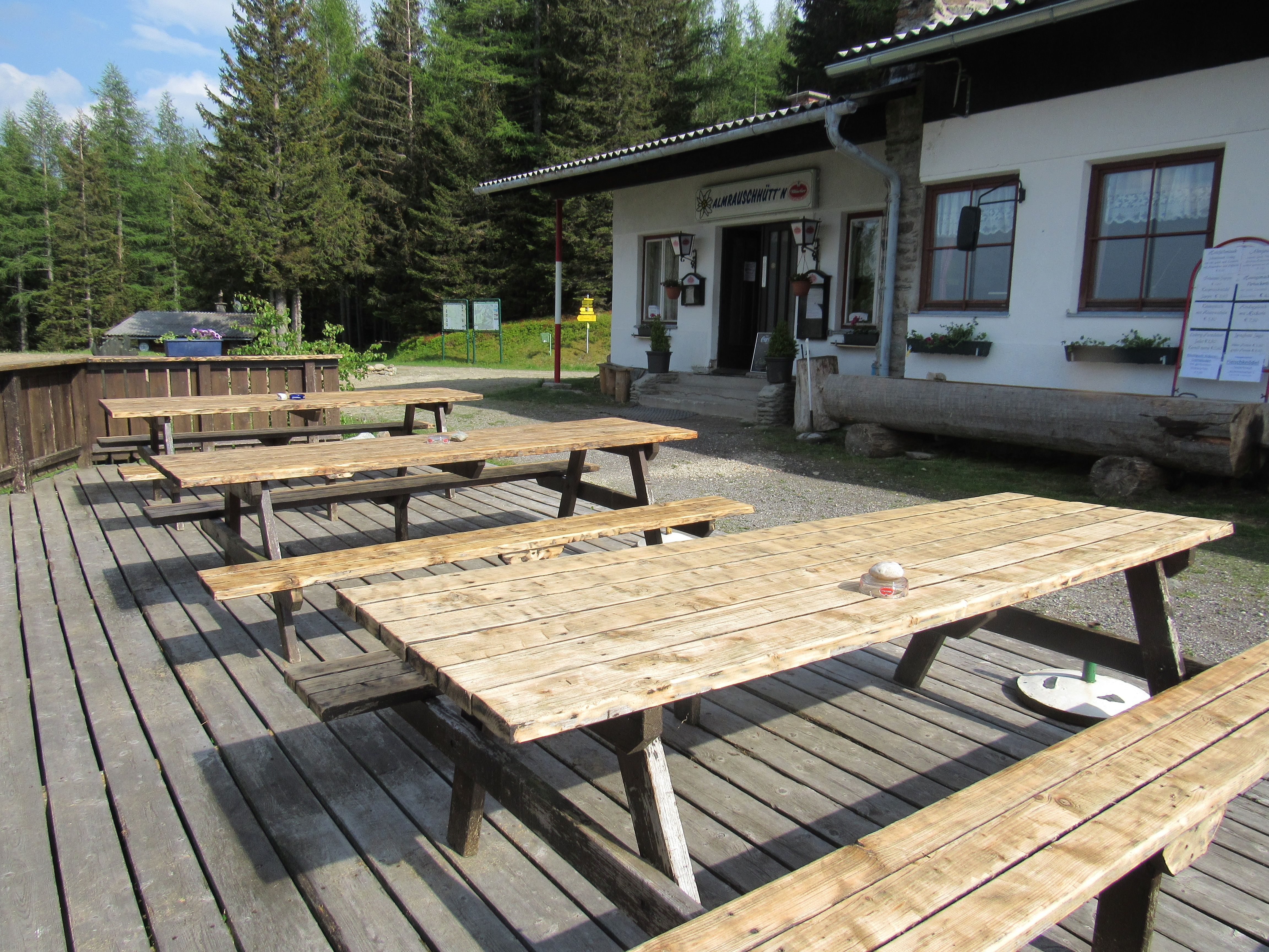 Wooden benches in front of the Almrausch hut in a wooded area.