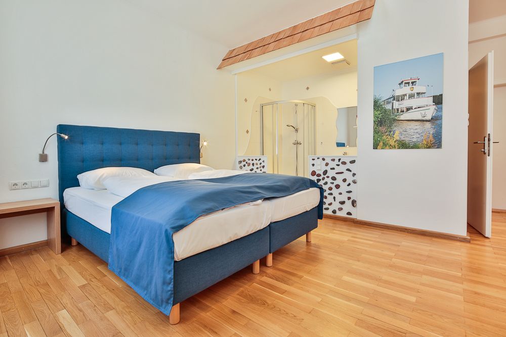 Hotel room with blue bed, wooden floor and open shower.