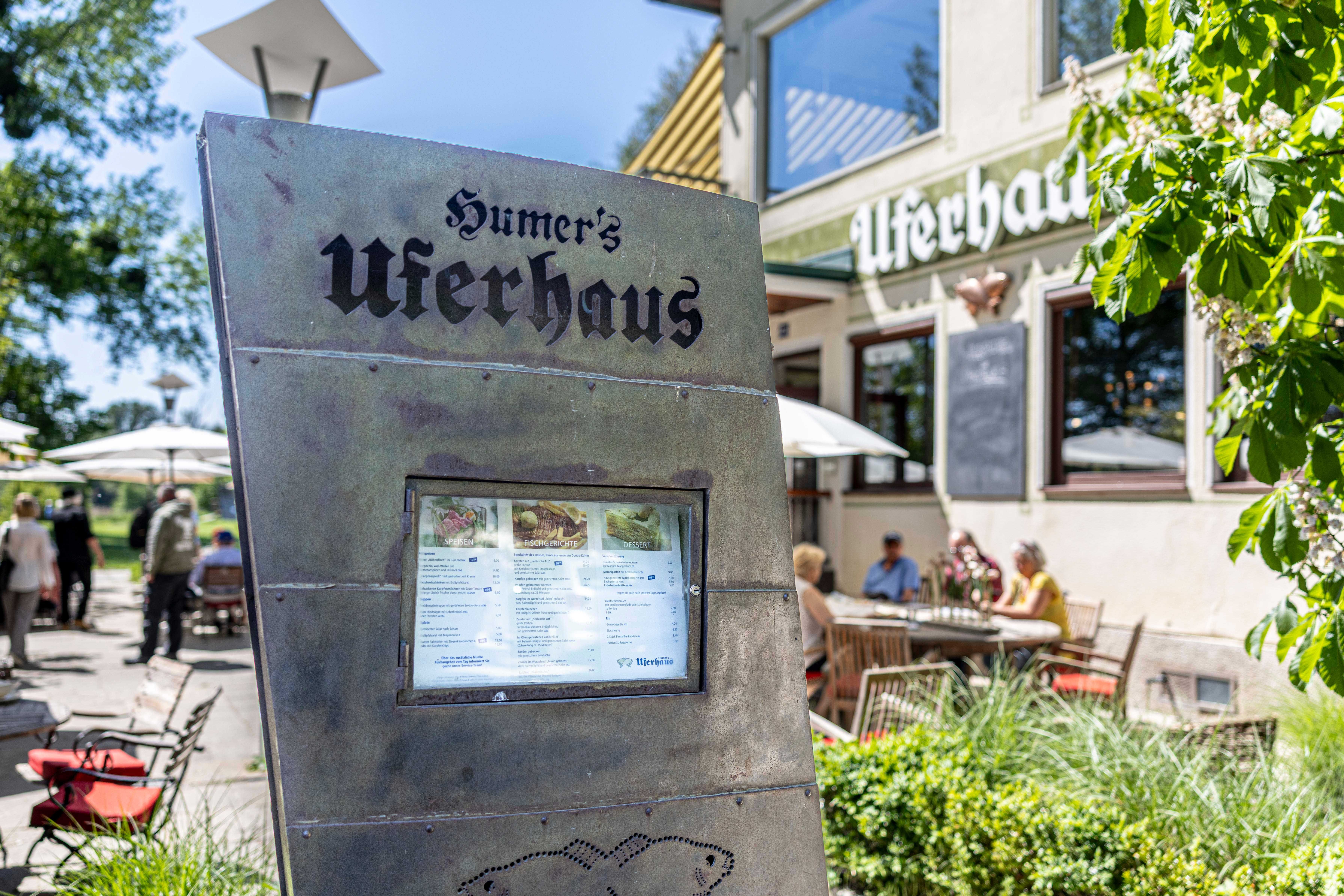 Exterior view of Humer's Uferhaus with menu in the foreground and guests in the background.