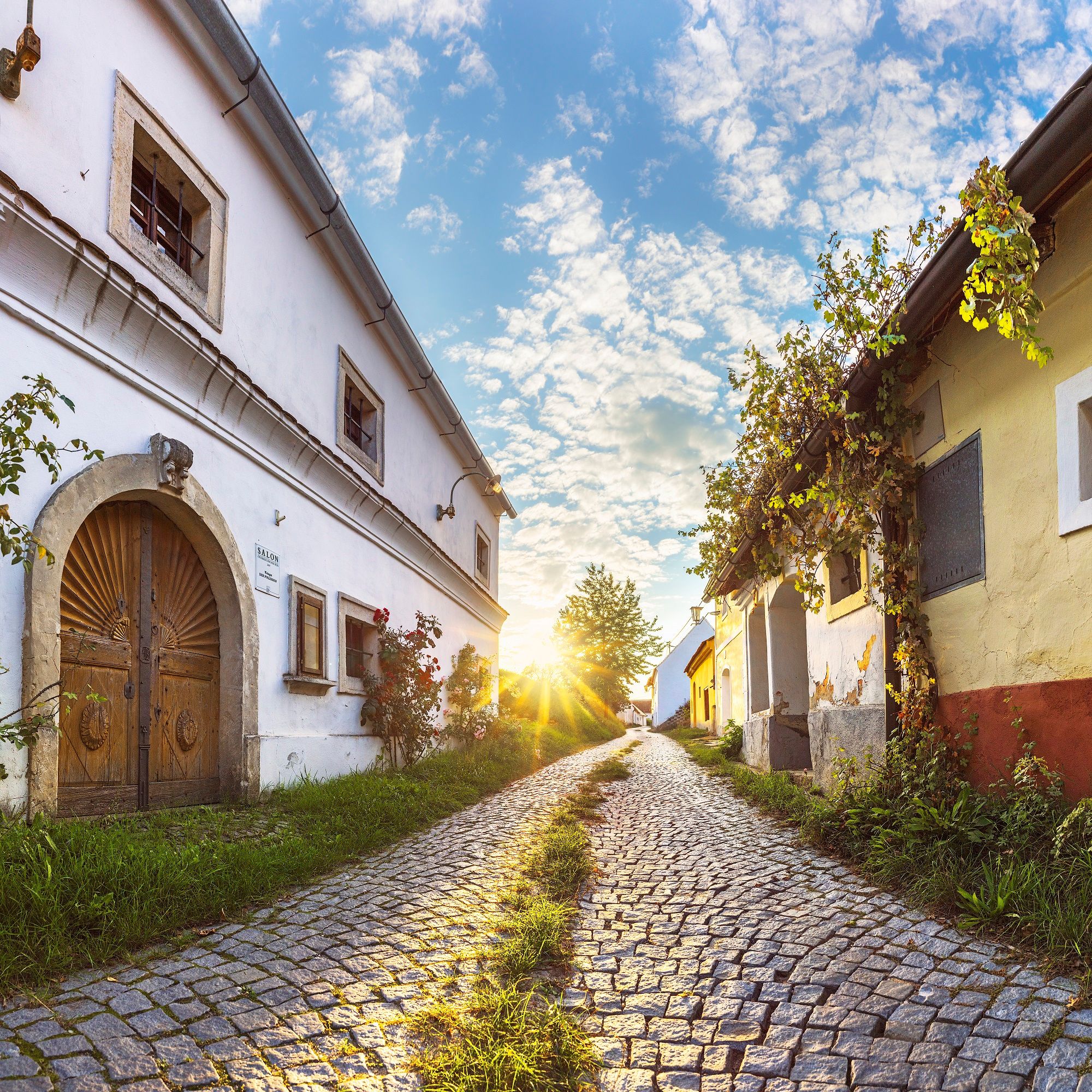 Cobbled street in Röschitz with traditional buildings and sunset in the background.
