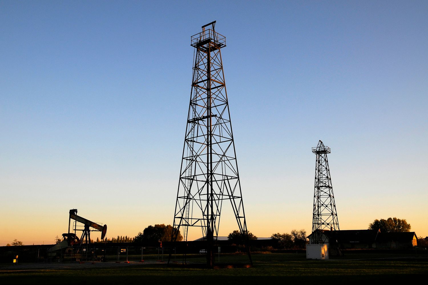 Two derricks and an oil pump at sunset.