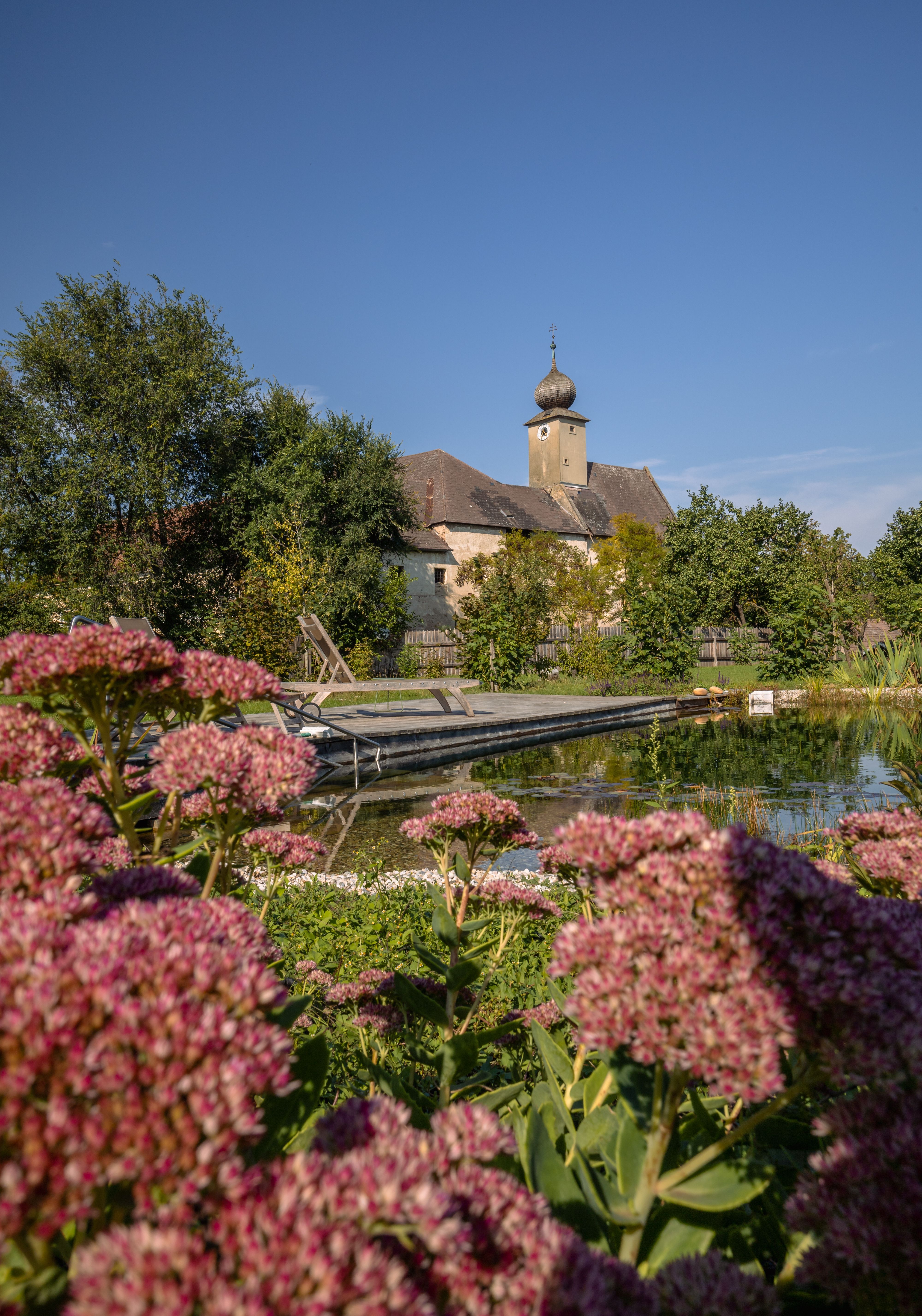 Bedroom with vaulted ceiling, wooden floor, bed, armchair, chest of drawers and fur rug.
