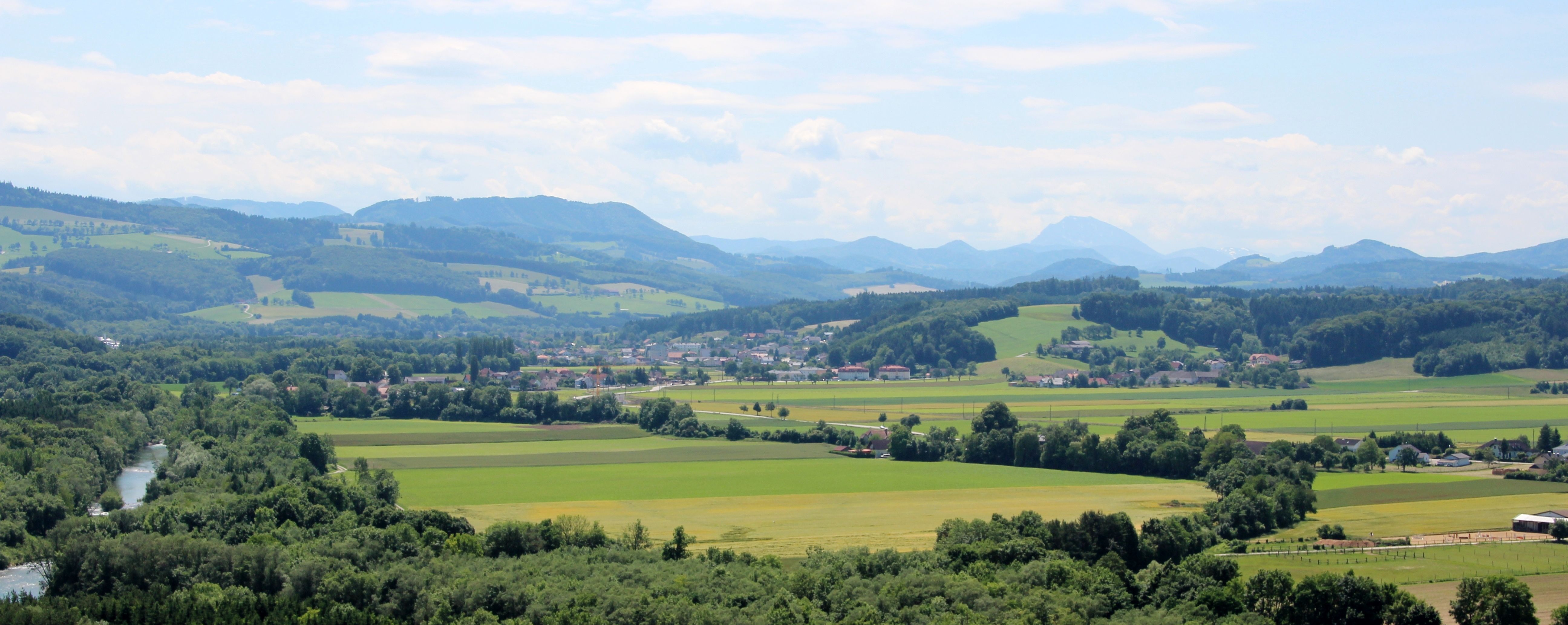 Panorama of a green landscape with hills, fields and a river.