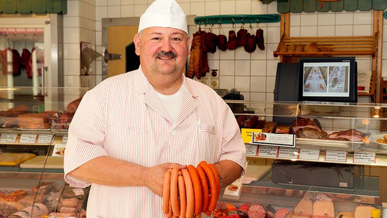 A man dressed in white holds sausages in a butcher's store.