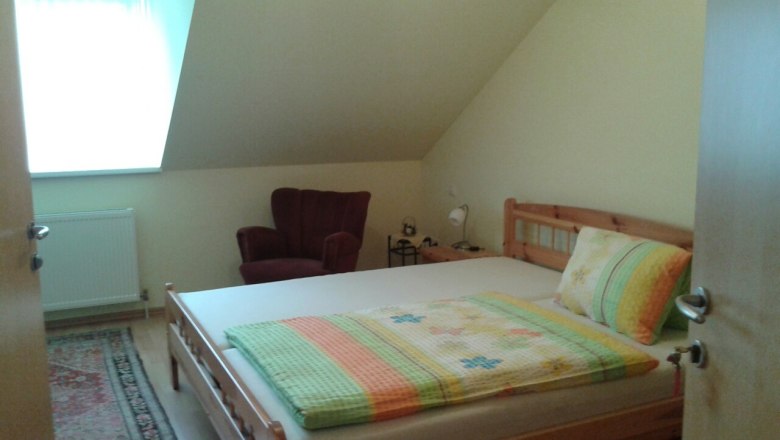 A cozy bedroom with a double bed, a red armchair and a small bedside table under a sloping roof.