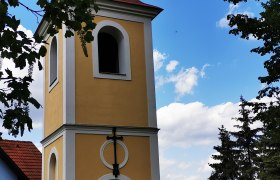 Bell tower in Ragelsdorf against a blue sky and trees.