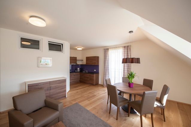 Modern living room with wooden floor, dining table and kitchenette.