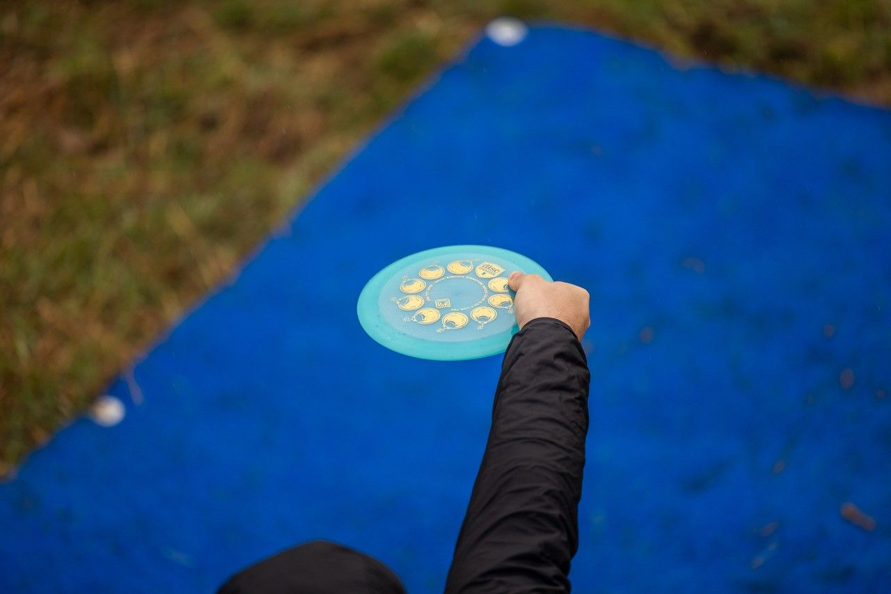 Person holds a disc golf target over a blue mat, hand outstretched for the throw