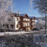 A snow-covered building with wooden balconies and surrounding trees in winter.