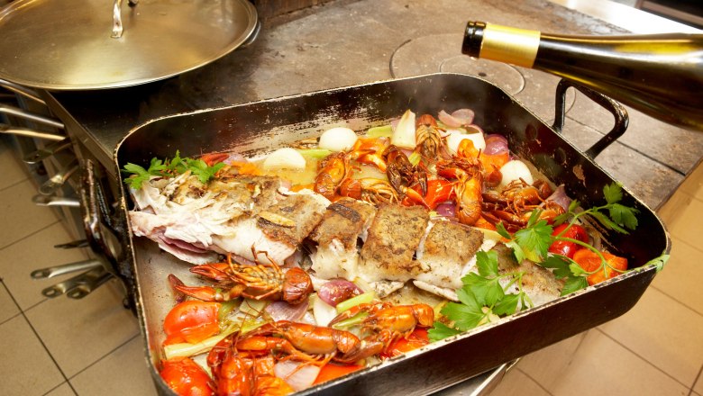 A roasting pan with fish, crayfish, vegetables and herbs on a stove.