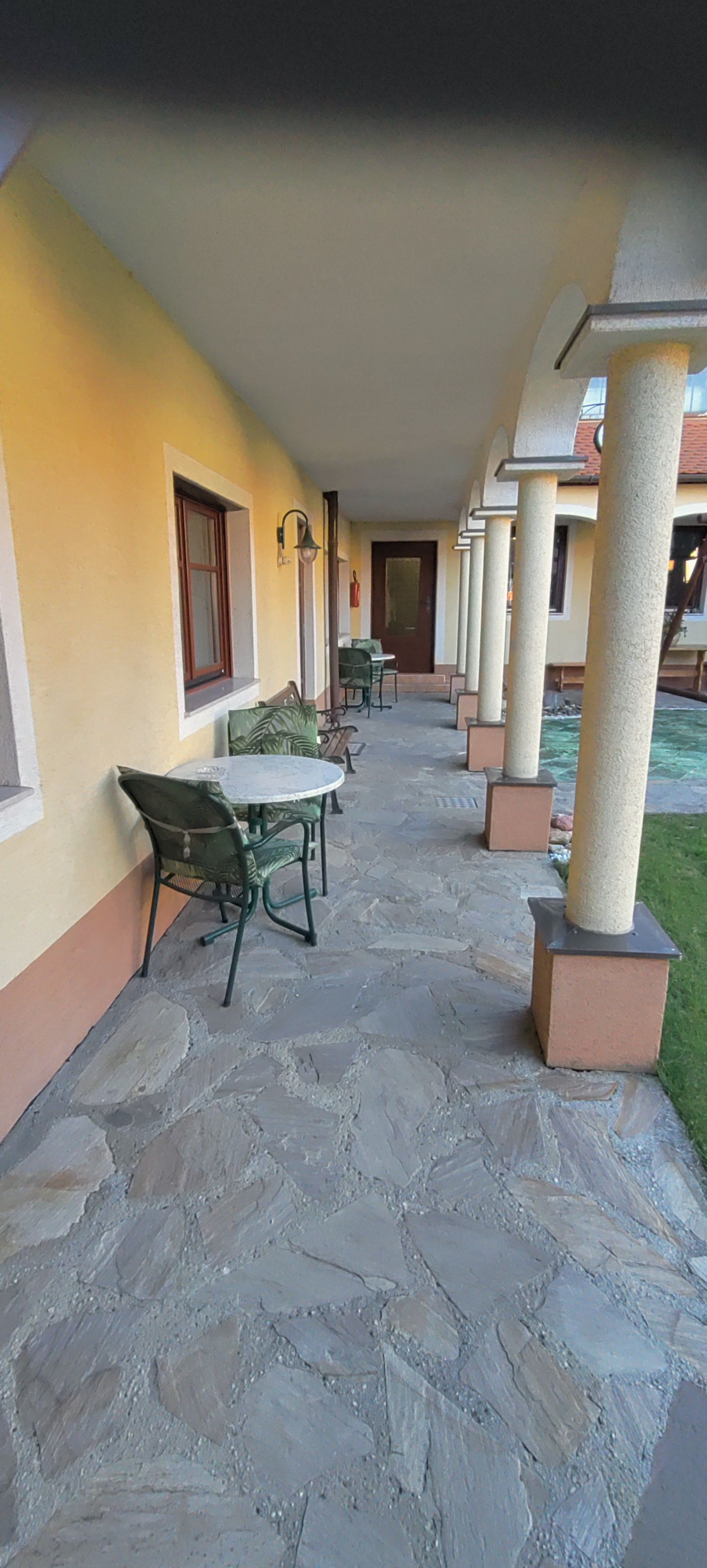 An arcaded courtyard with a stone floor, yellow wall and columns. Tables and chairs are placed along the wall.