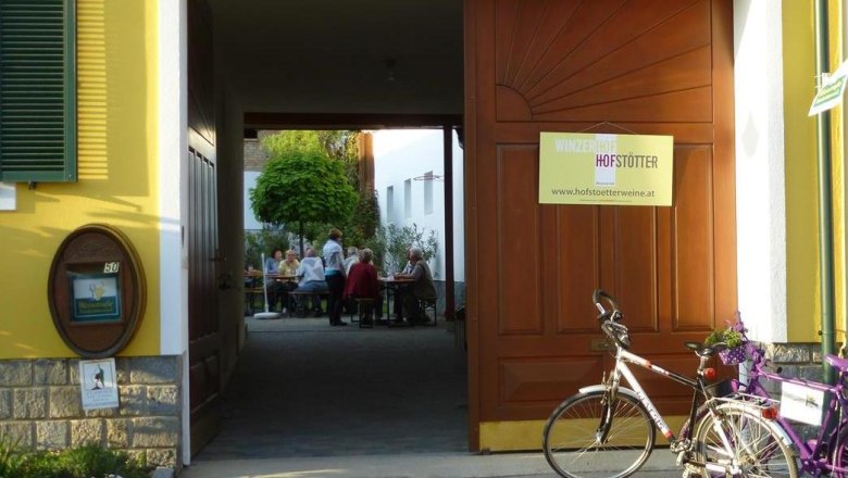 Entrance to a winery with an open gate through which you can see people sitting at tables. A bicycle is parked in front of it.