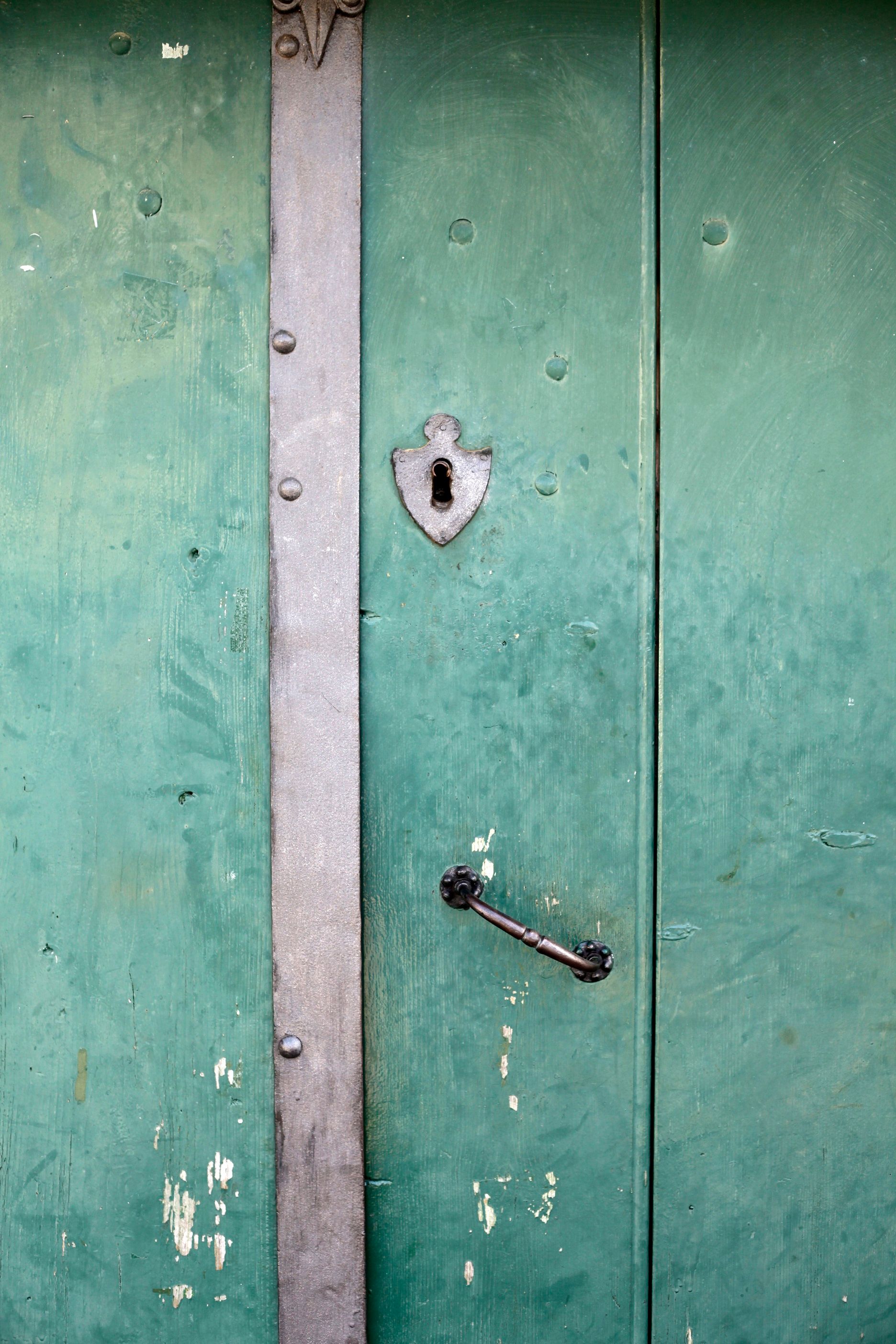 Green wooden door with metal fittings and a keyhole.