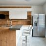 Modern kitchen with wood and white tones, bar stools and stainless steel fridge.