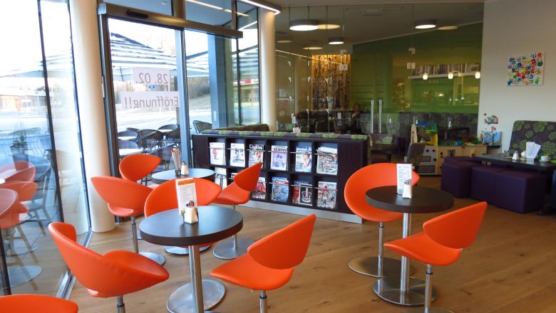 Interior view of a modern café with orange chairs and magazine rack.