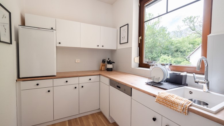 Modern kitchen with white cupboards, wooden worktop and large window with a view of the greenery.