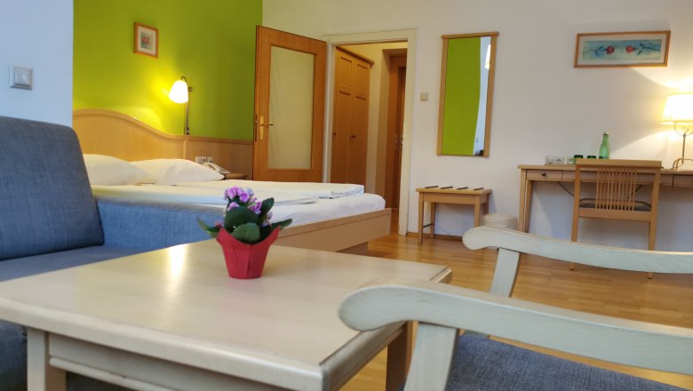 Hotel room with green accent, bed, desk and armchair.