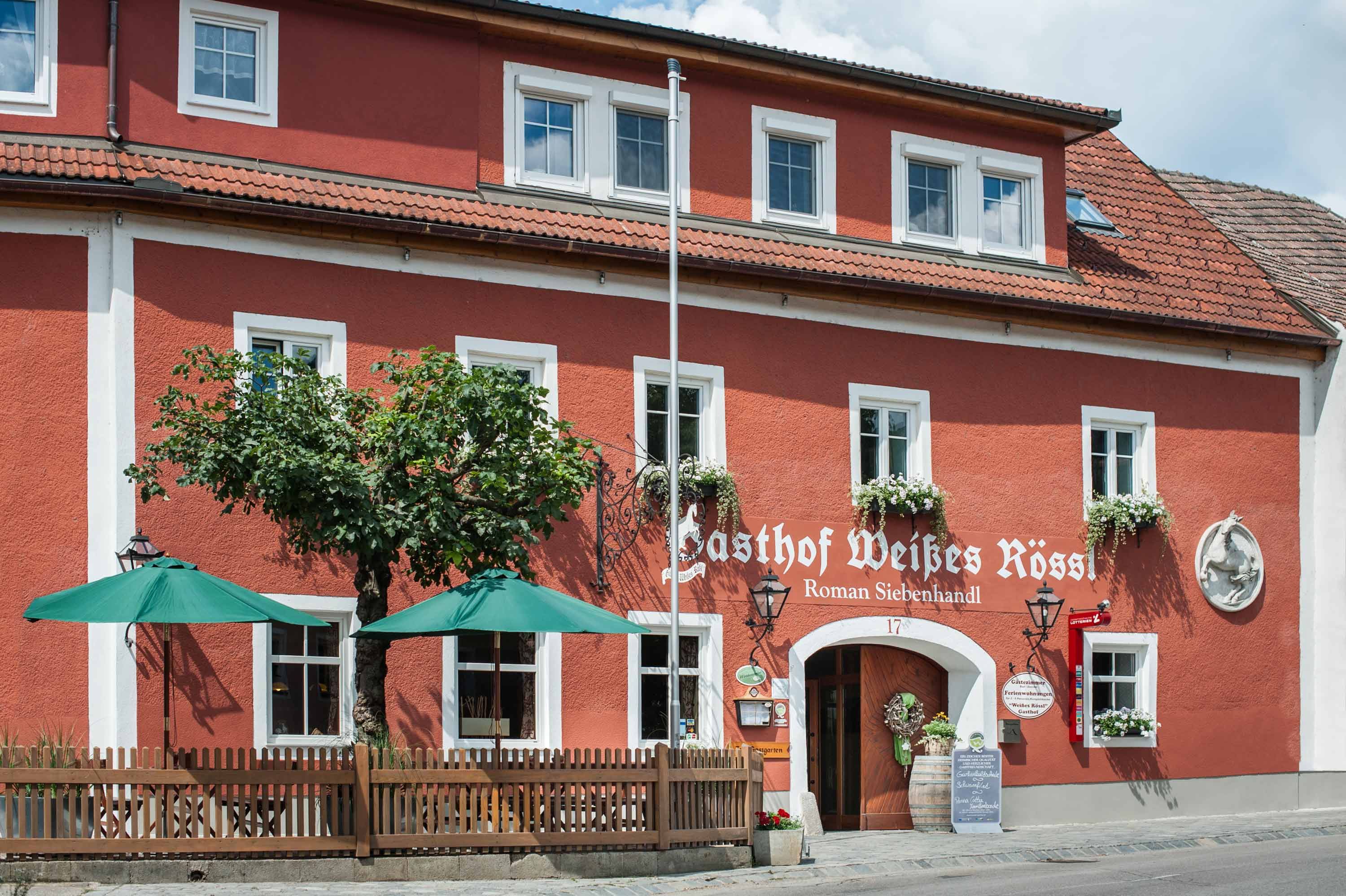 Red building with white window frames and green parasols in front of the entrance.