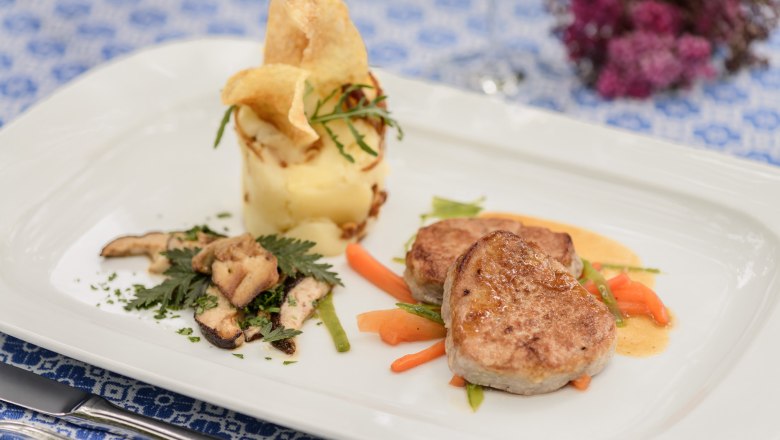 Gourmet dish with meat, mashed potatoes and vegetables on a white plate.