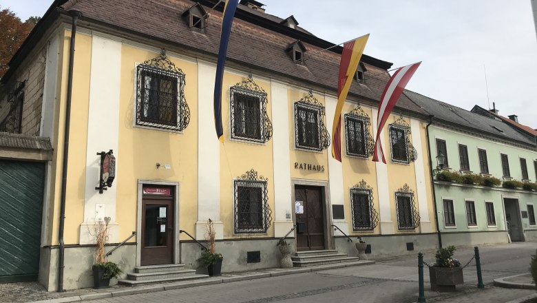 The Persenbeug town hall with its yellow façade and decorative window grilles, decorated with flags.