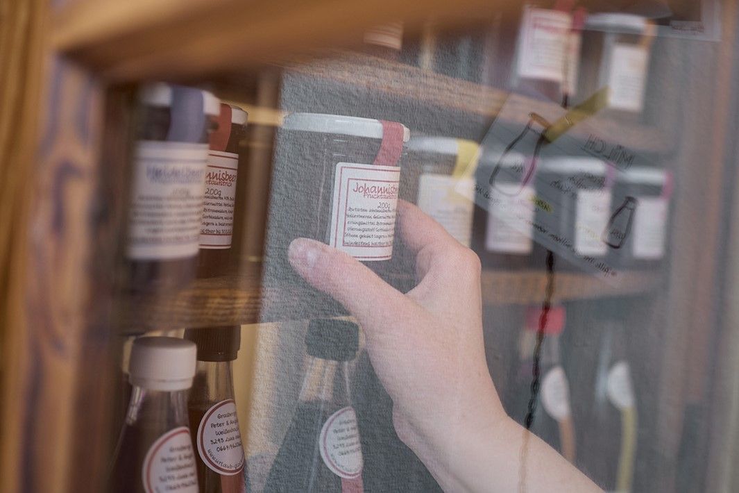 A hand reaches for a jar of homemade redcurrant jam on a shelf.